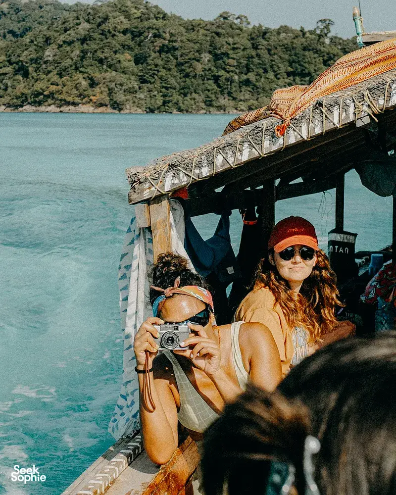 Traveller on a longtail boat photographing the Andaman Sea as Moken guides take guests out to Surin Island from Khao Lak