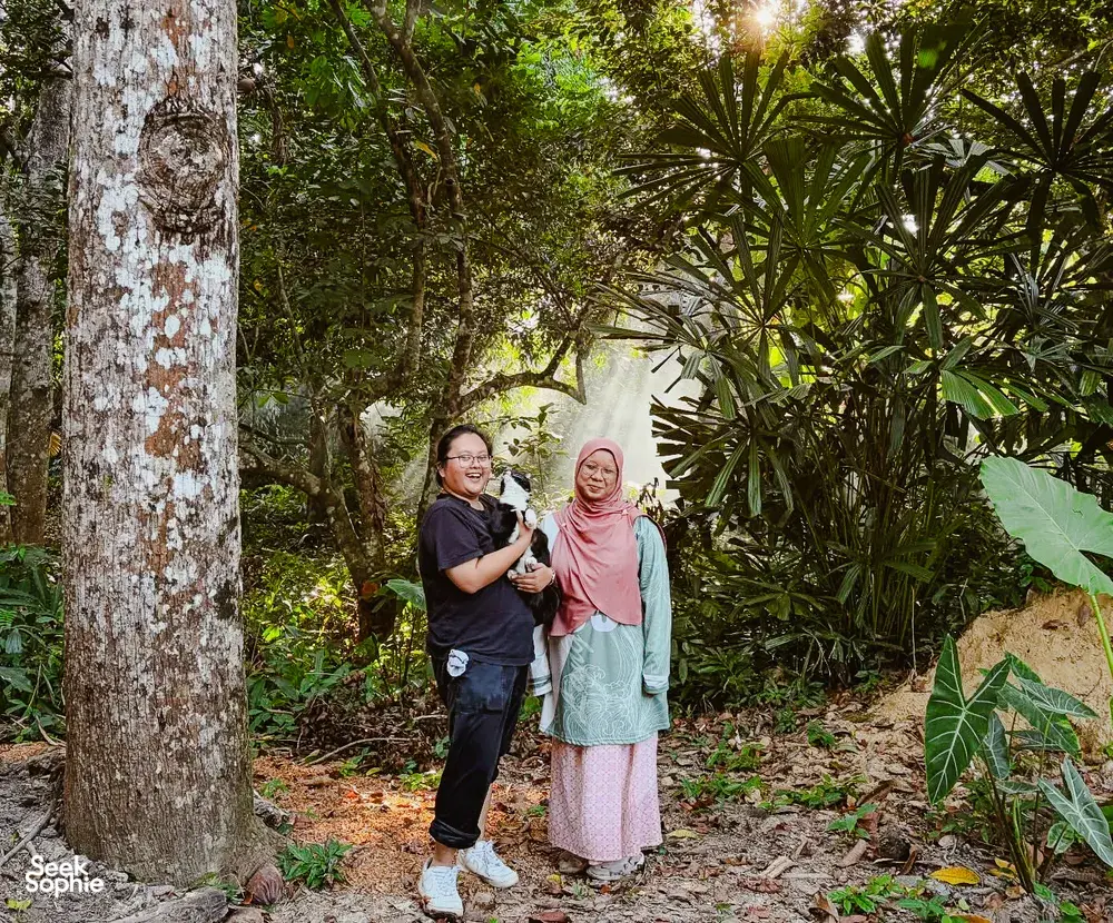 Two travellers standing in a shaded garden at Kebun Lidstari in Langkawi, surrounded by palms and dense tropical greenery