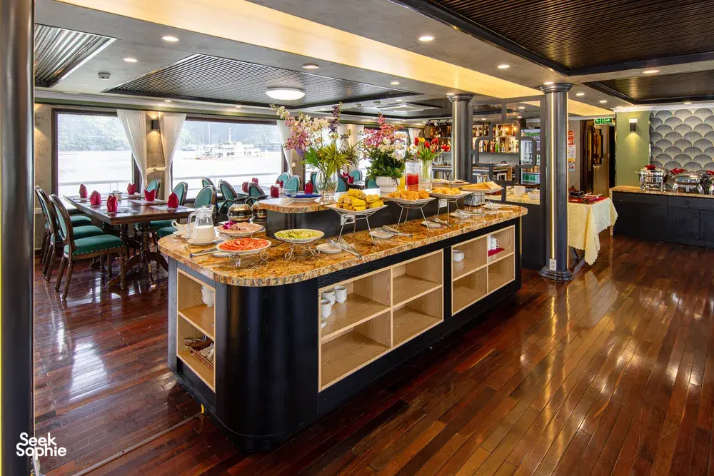 Buffet restaurant on the Oasis Bay Party Cruiser with chafing dishes, fruit and drinks set out for guests on Halong Bay