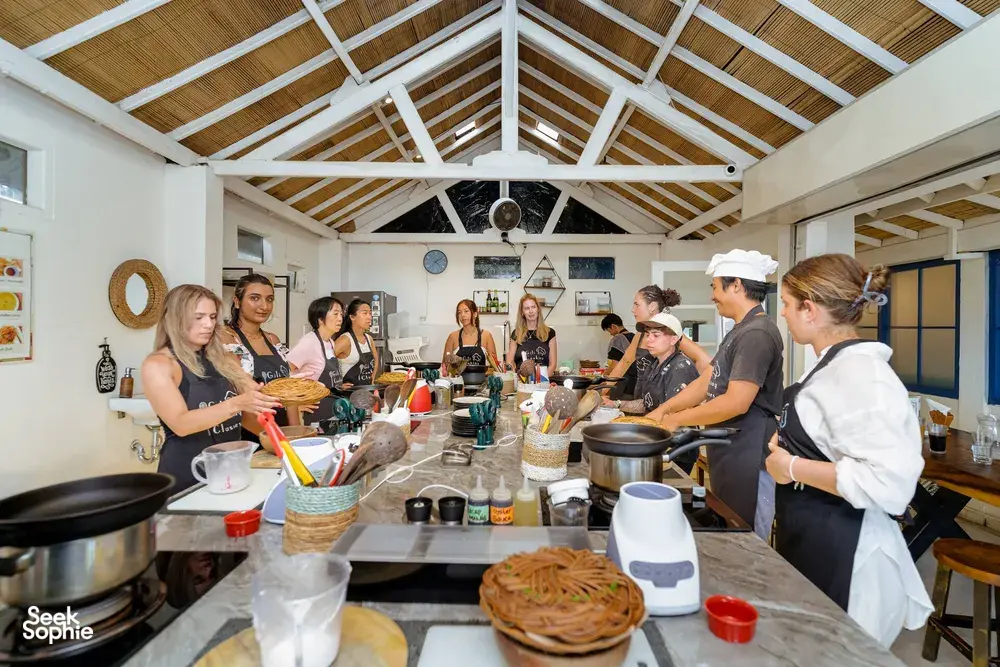 Small group Indonesian cooking class on Gili T in Lombok gathered around pots and utensils under a high white ceiling