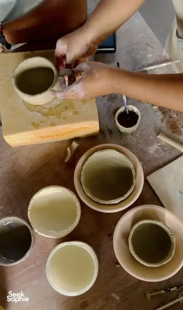 Hands glazing ceramic cups and bowls on a pottery table at Ilham Ceramic Studio in Langkawi’s village workshop