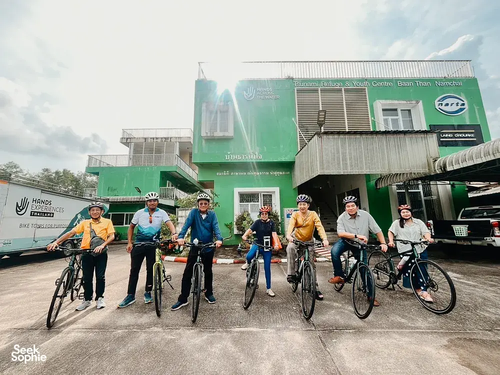 Helmeted cyclists posing outside a Hands Experiences Thailand centre in Khao Lak, ready for a half-day cycling and rafting trip