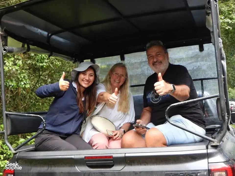 Three visitors smiling and giving thumbs-up inside an open safari jeep on the way through Khao Yai National Park forest