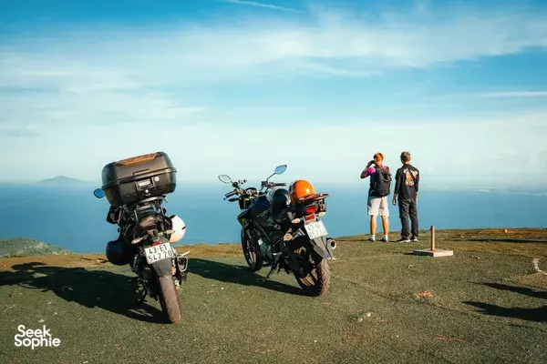 Da Nang sunset motorbike adventure: two parked bikes and travellers standing on a hilltop lookout overlooking the sea