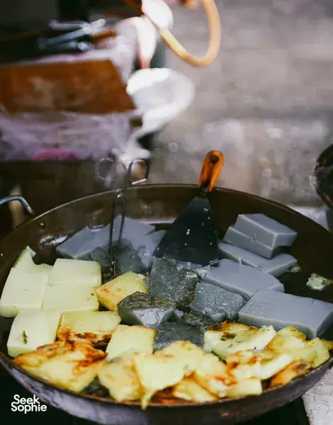 Sizzling wok of fried tofu and batter in a smoky Lijiang stall, capturing the flavours behind a local food hunt