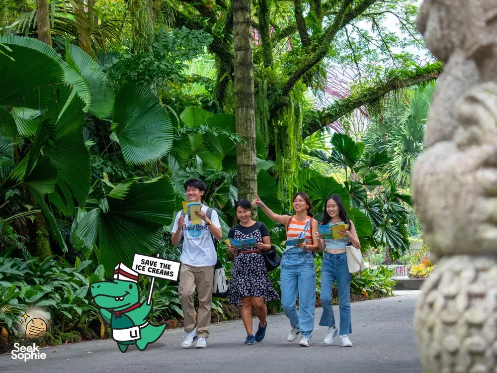 Group strolling along a lush garden path during a Singapore puzzle hunt for teams, carrying clue props and following the route