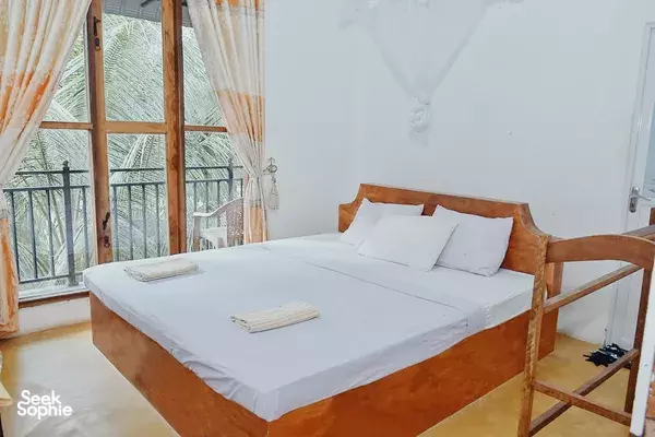 Sunlit lodge room with a wooden double bed, white sheets and orange curtains, inside Splendid Lake View Safari Lodge, Udawalawe