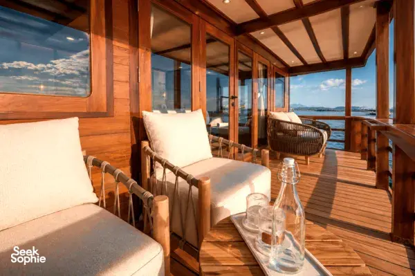 Wooden phinisi deck lounge with beige armchairs, a small table and sea view, during a Komodo group cruise in Labuan Bajo