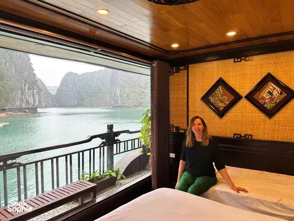 Anh relaxing on a bed inside a wooden cabin as karst islets unfold outside the window on Halong Bay