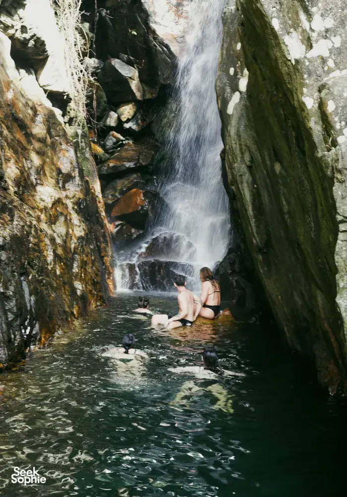 Swimmer relaxing in a narrow waterfall pool between jungle cliffs on a secret waterfall outing from Hoi An