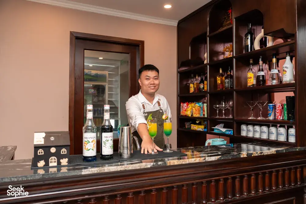 Sunshine Golden Cruises staff member pouring drinks behind the bar aboard a luxe 2D1N Cat Ba cruise during evening service
