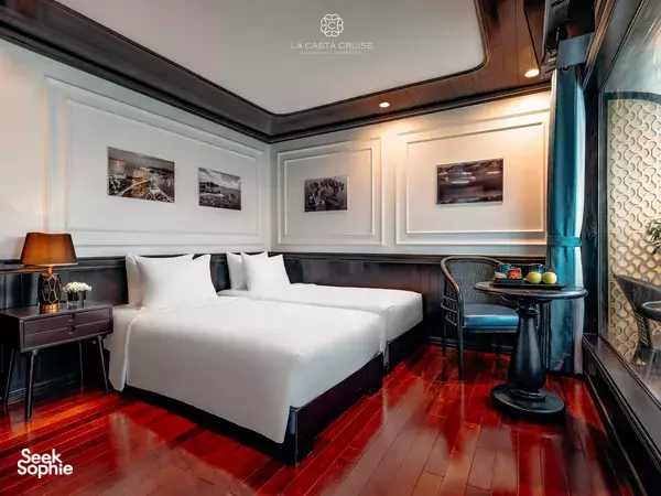 La Casta cruise cabin bedroom with a large double bed, bedside tables, and seating by the window, onboard in Halong Bay