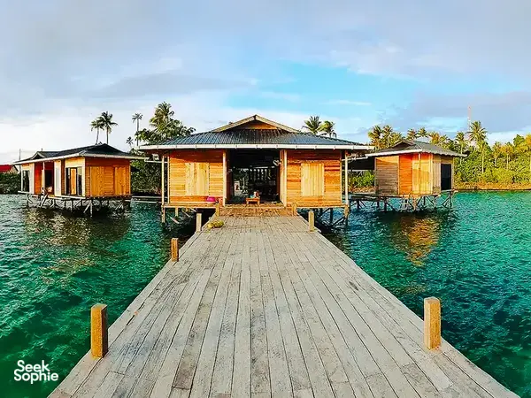 Timber overwater walkway leading to wooden chalets at Luma Selakan sea lodge in Semporna, surrounded by clear green sea