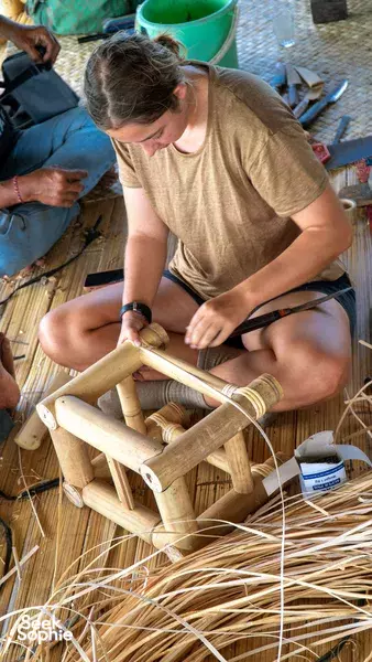 Bamboo Creative Bali in Bali: a woman trims a bamboo frame with a hand tool while others work nearby in a workshop.