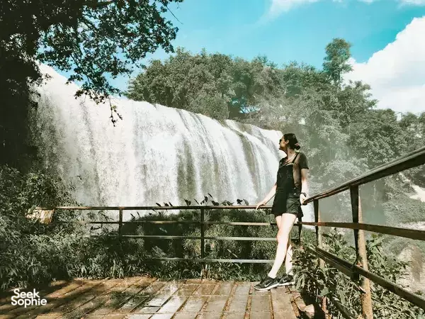 Traveller stands on a viewing deck by a wide waterfall near Da Lat during the Easy Rider route to Mui Ne