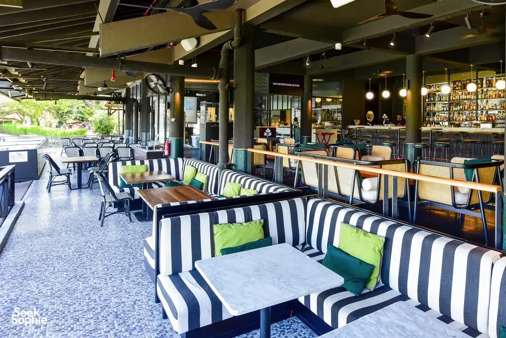 Striped bench seating and arched patio tables beside a well-stocked bar in a Singapore team cooking challenge venue