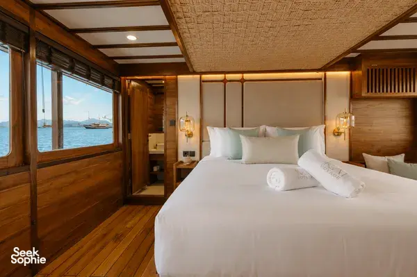 Travass Life new phinisi double cabin with a made bed, warm lighting and an ocean view through the window on a Komodo Island trip