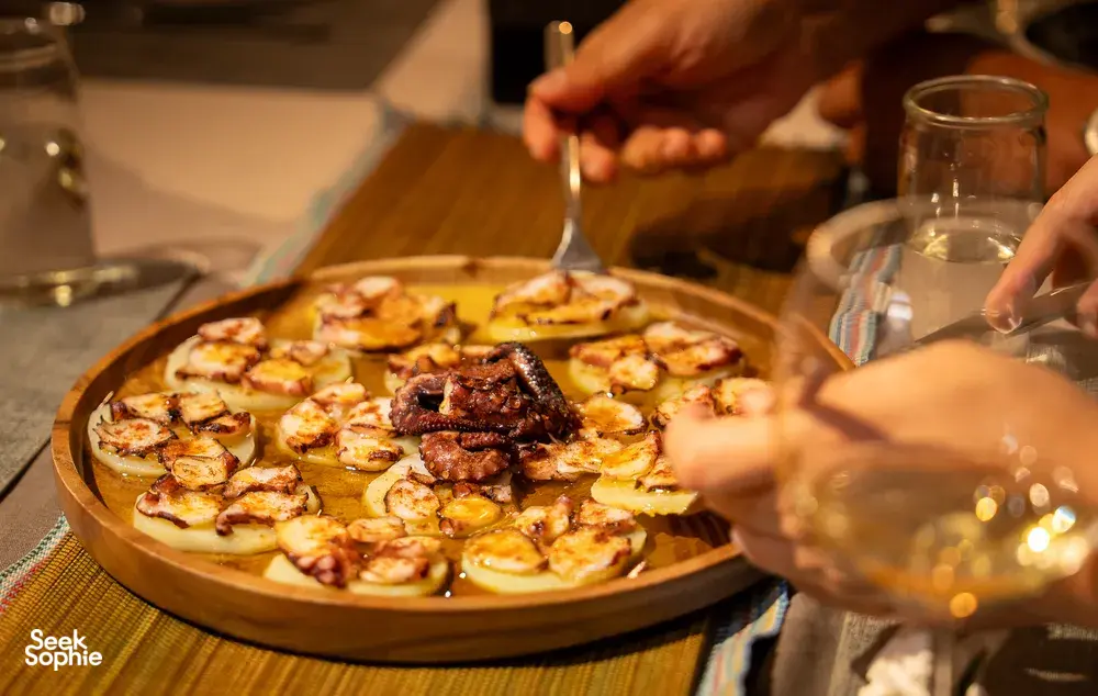 Large tapas tray of bite-sized dishes as guests eat together, with hands reaching in at home table during private dining Singapore
