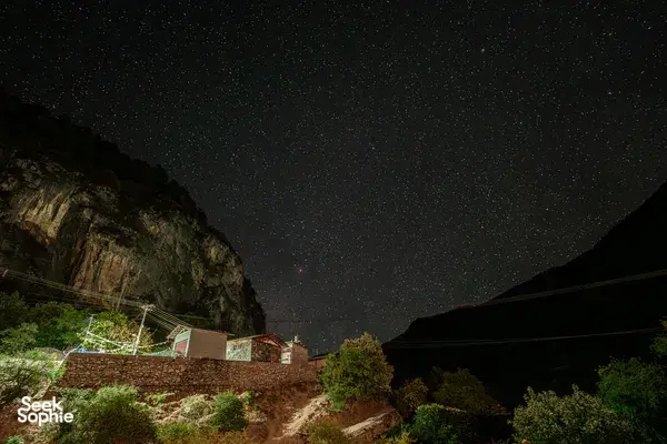 Starry night sky over Shangri-La mountains and valley village rooftops with power lines below at night