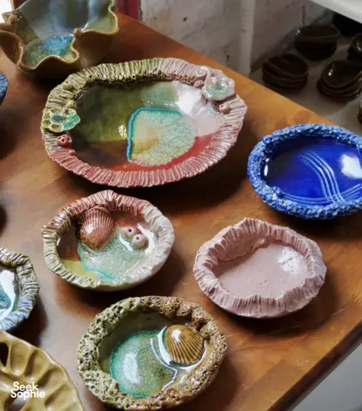 Handmade ceramic bowls and plates in green, pink and blue glazes arranged on a wooden table at Ilham Ceramic, Langkawi.