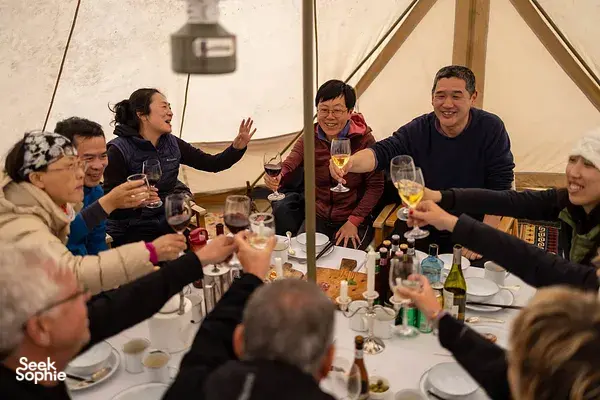 Group dinner under a large canvas tent with friends raising glasses around a table of wine and candles, China