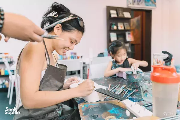 Ukulele painting session at Avant-Garde Art Space in Singapore, a participant paints at her station while an instructor helps