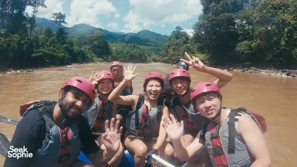 Group selfie on an inflatable raft, pink helmets visible, on the Padas River with lush hills behind during Xtreme Paddlers rafting