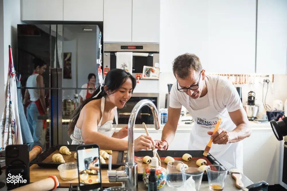 French Cooking Lab chef guiding croissant dough shaping at the counter in a bright Singapore kitchen baking class