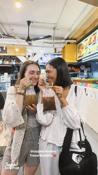 Two travellers smiling and sipping drinks inside an eatery during a private night walk in Geylang, Singapore — Singapore hidden gems