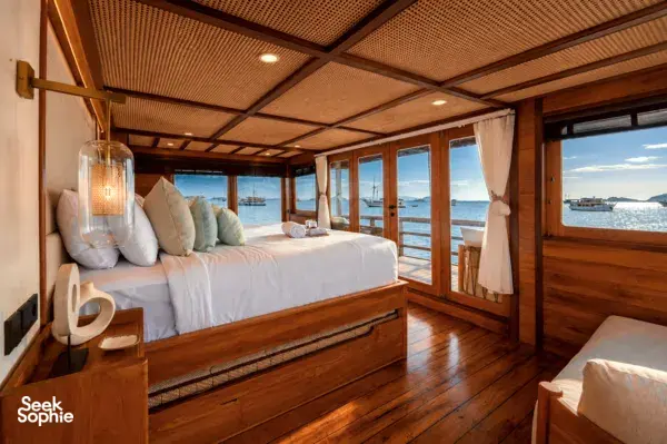 Cozy phinisi cabin with a made bed, throw pillows and ocean-facing windows, set for relaxed 3D2N shared Komodo Island