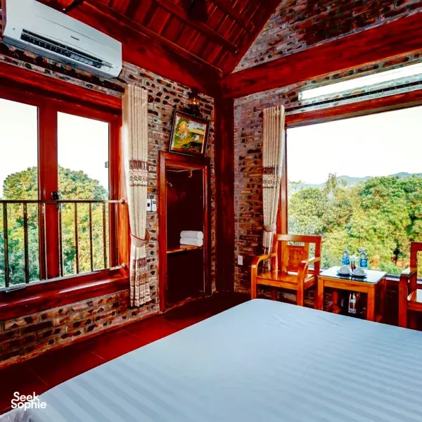 Cozy bedroom inside a Ninh Binh homestay, red timber ceiling and brick walls with two windows overlooking countryside