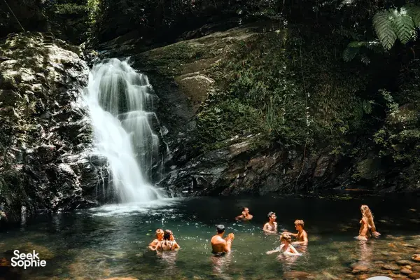 People swimming in a natural pool beneath a forest waterfall at Bach Ma near Da Nang on a Connect Travel camping trip