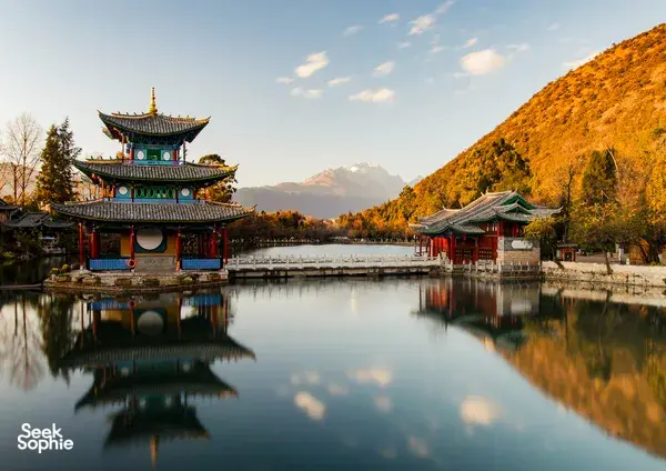 Historic lakeside pavilion and gate across calm water, with towers and autumn hills glowing at golden hour in Northern Yunnan