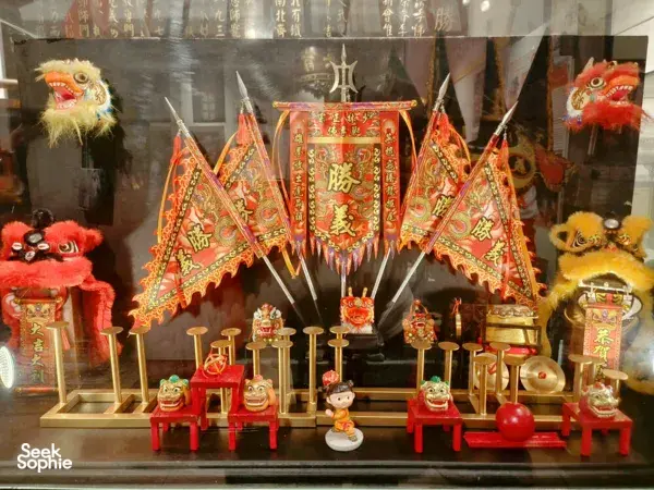 Lion dance headpieces, small guardian lion figures and an ornate red ceremonial banner displayed in a Ho Chi Minh City kung fu room