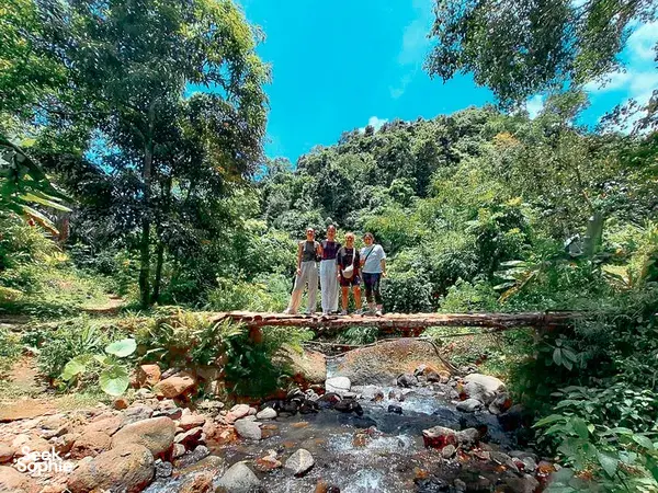 Walkers pause on rocks beside a shallow stream in the Lombok jungle during the Lombok Forest Tour forest walk