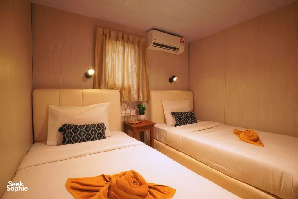 Two single beds in a cosy Seaventures Dive Rig cabin, with orange towel wraps, an air conditioner and warm light