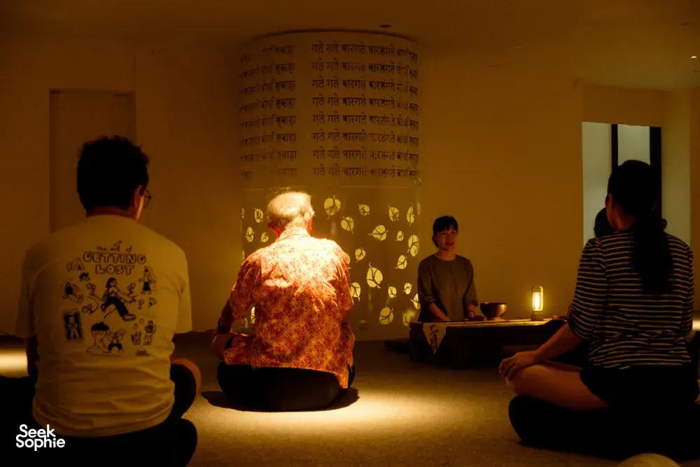 Participants sit on the floor as a host presents agarwood scents in a lantern-lit workshop room in Hanoi
