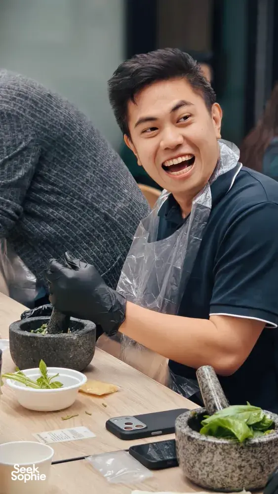 Smiling facilitator in gloves crushing basil for pesto in a stone mortar on a lunch table, Singapore workshops in Singapore
