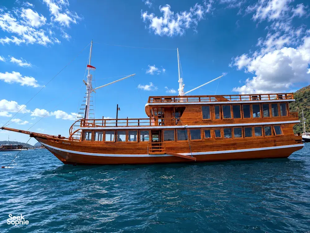Wooden Phinisi cruising on blue open water with tall masts under dramatic clouds on a 3D2N shared Komodo cruise, Labuan Bajo