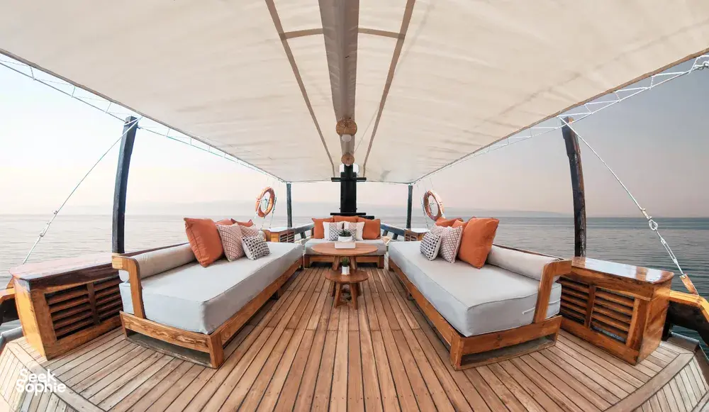 Sun deck with cushioned daybeds and a central table on a private 3D2N Komodo liveaboard, cruising near Labuan Bajo