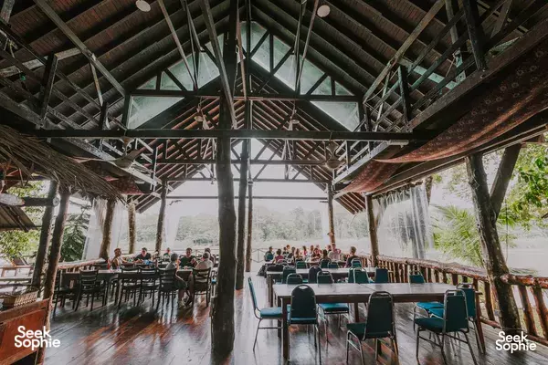 Rows of green chairs set under a wooden pavilion at Scenic Riverside Resort, with sheer drapes and views to the Kinabatangan River
