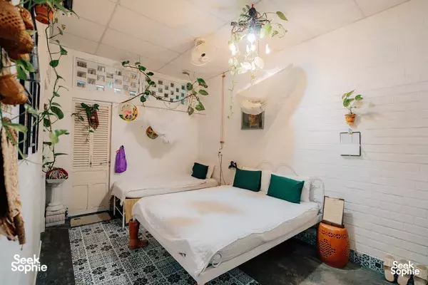 Cosy bedroom in a pottery homestay in the Mekong Delta, with a white bed, green cushions, and hanging plant décor
