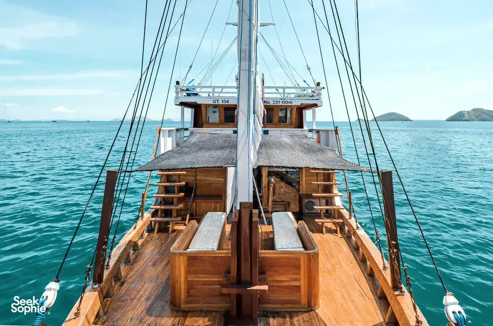 Private 3D2N Komodo cruise on a sleek white phinisi: view down the wooden bow deck with sails and sea in Labuan Bajo