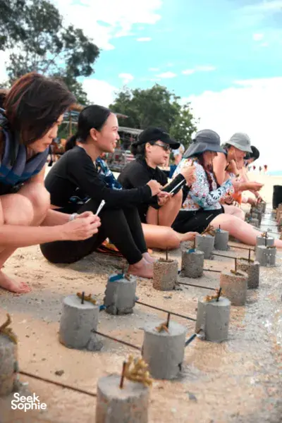 Travellers kneeling in shallow water filling coral planting frames with cement during the Rinca Coral Nursery Program on Komodo Island