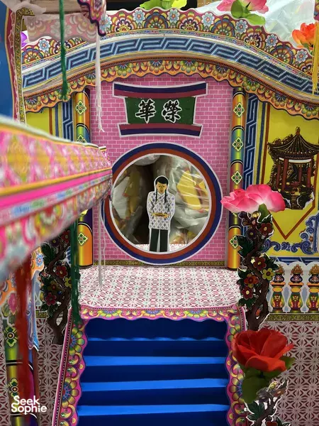 Decorative shrine arch with Chinese characters framing a white paper deity figure on blue steps, inside a Singapore tradition workshop