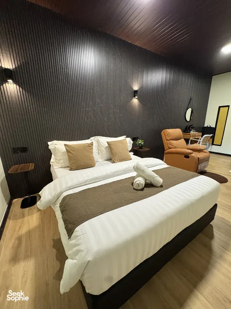 Double bed with stacked pillows and a lounge chair in a modern guest room at Sukau Greenview Lodge, Sandakan, Kinabatangan River