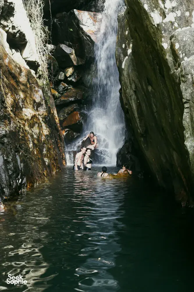 Swimmers in a misty hidden waterfall gorge, surrounded by steep cliffs on a secret waterfall trip from Hoi An