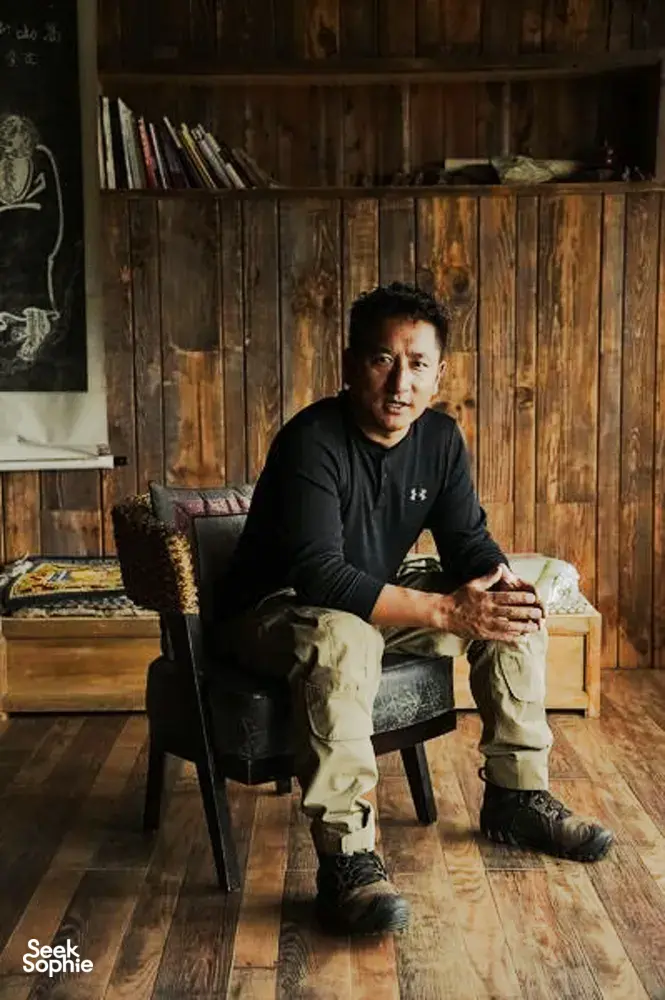 Khampa Caravan host seated in a rustic wooden room in Shangri-La, meeting Tibetan cultural guide during a home visit