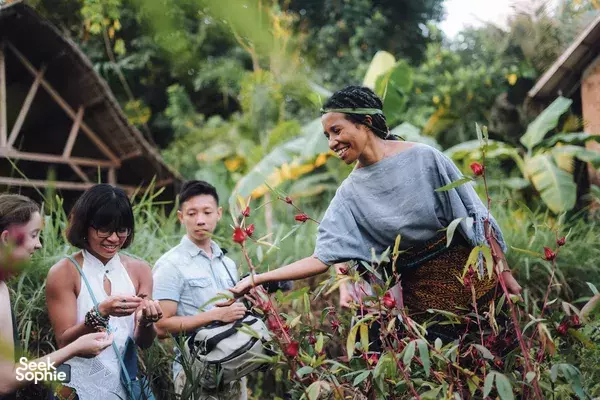 Local guide in a headscarf leads guests through dense greenery, pointing at plants during a garden stop, Labuan Bajo