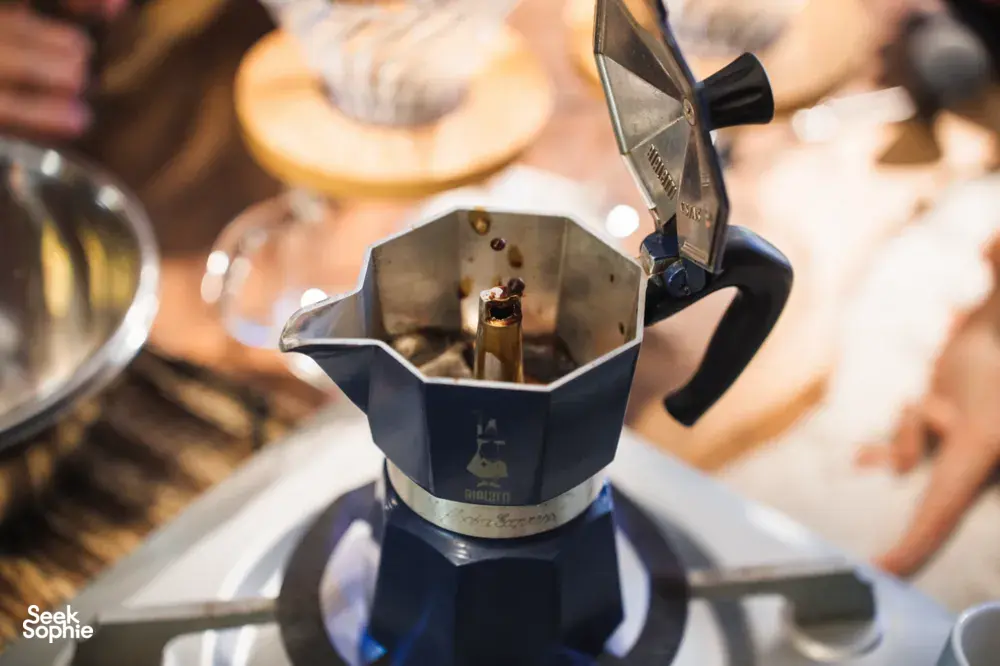 Close-up of dark coffee beans falling from a metal roaster hopper onto a burner during a hands-on workshop — workshops in Singapore